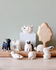 A collection of Handmade Tiny Wooden Forest Animals - Bunny by Bali artisans, including a panda, deer, tortoise, and cats, displayed on a wooden surface against a muted green wall.
