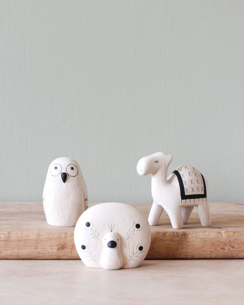 Three hand-painted tiny wooden exotic animals—a seal, an owl, and a sheep—decoratively painted in a minimalist style, displayed on a wooden ledge against a pale green background.