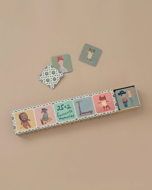 A rectangular Maileg Memory Game box, opened on a beige background, reveals three illustrated cards with Dorthe Mailil's charming animals and characters, inviting you to enjoy a nostalgic game of recollection.