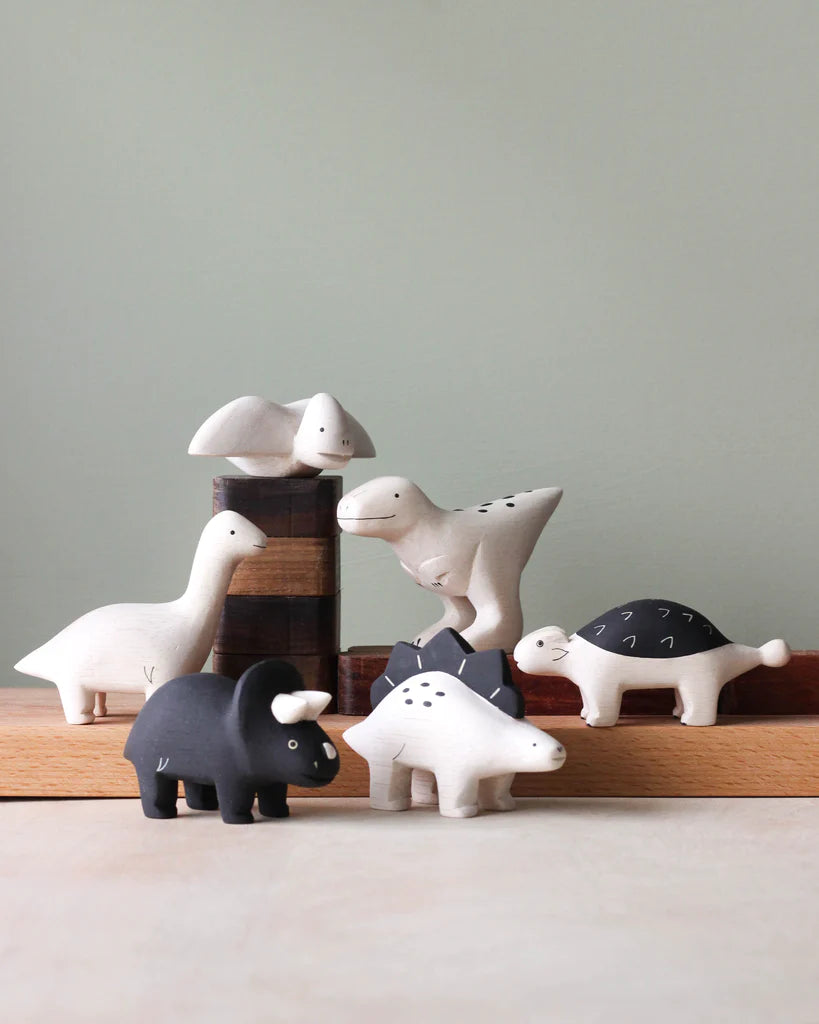 A collection of hand-painted wooden animal figurines, including birds, a "Handmade Tiny Wooden Dinosaurs - Stegosaurus", and various mammals, displayed against a soft grey background.
