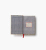 An open Schoolhouse Mini Embroidered Journal with a blue and white gingham inner cover, unlined pages ideal for free writing or sketching, and a red ribbon bookmark. A label reading “Journal” appears on the right page. The background is plain white.