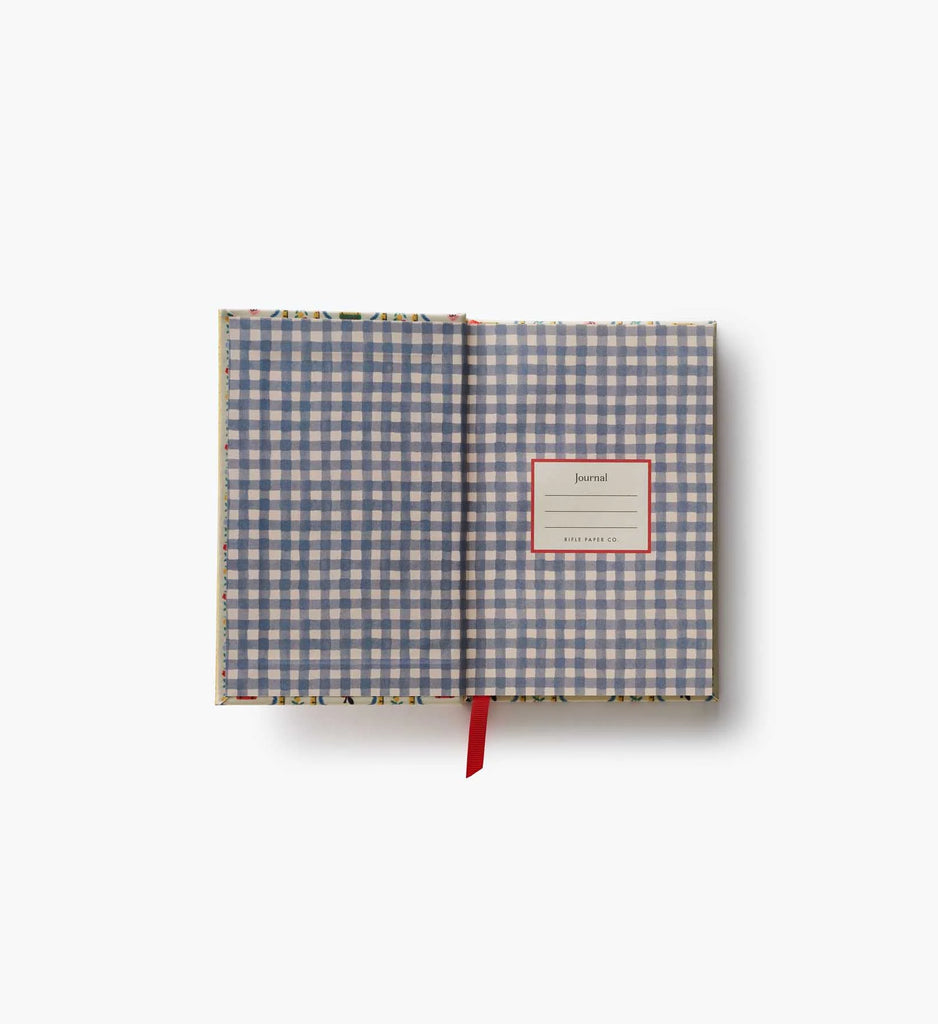 An open Schoolhouse Mini Embroidered Journal with a blue and white gingham inner cover, unlined pages ideal for free writing or sketching, and a red ribbon bookmark. A label reading “Journal” appears on the right page. The background is plain white.