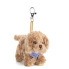 The Bukowski - Kharma Dog Bag Charm features soft brown fur, a blue and white checkered bow tie, and a metal clip on a tan strap. Photographed against a white background, this charming plush dog keychain is an adorable accessory that adds playful style to any bag.