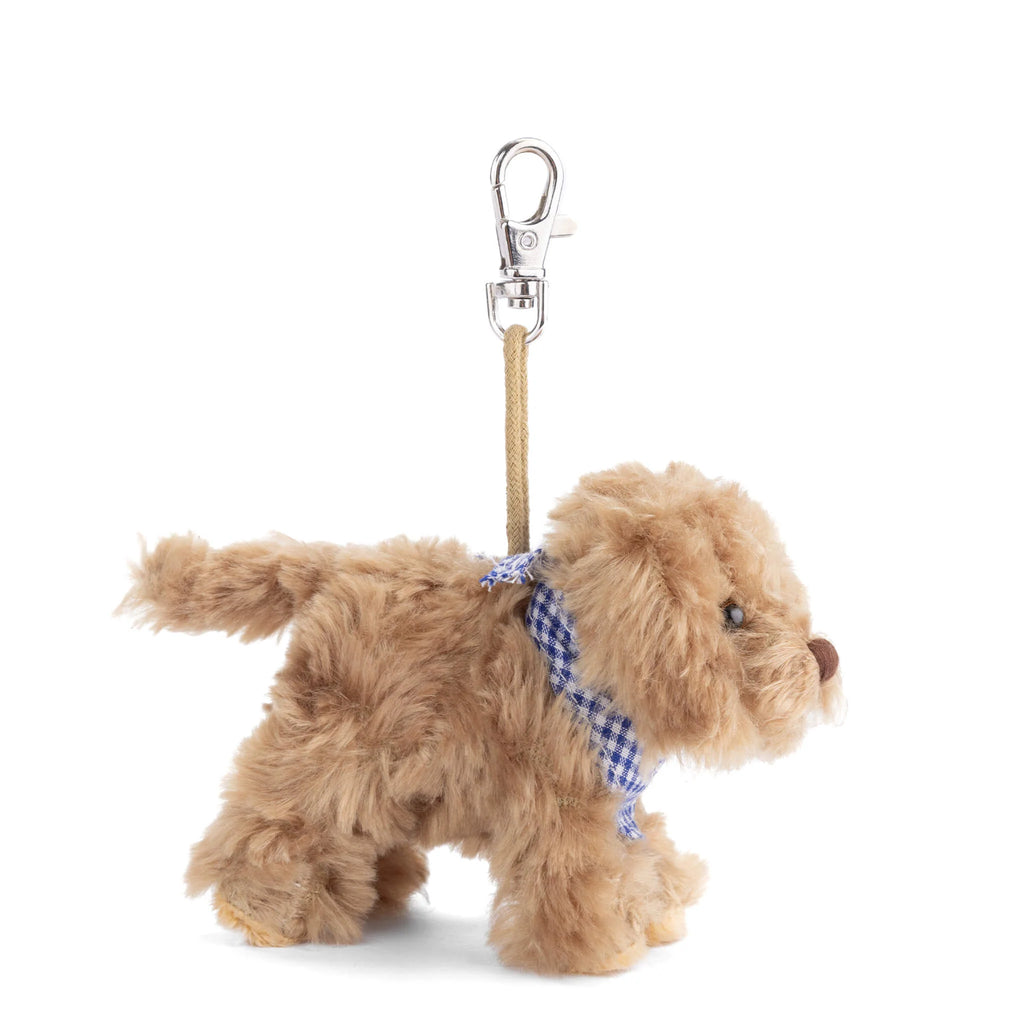 Bukowski - Kharma Dog Bag Charm features a plush dog with light brown fur, accented by a blue and white checkered ribbon collar and a leash with a metal clip attached to its back—making it the perfect cute plush accessory or charming puppy bag charm.