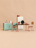 A Maileg Kitchen Set featuring a light green sink, a tall refrigerator, and a school table with two chairs, all arranged with toy food, a waffle iron, and kitchen accessories.