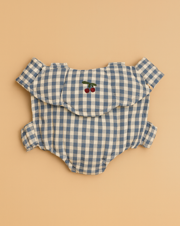 The Konges Sloejd Doll Carrier in Blue Checkers, shown beside a blue and white gingham baby romper with ruffled sleeves and cherry embroidery, makes a charming cotton accessory for your child's doll.