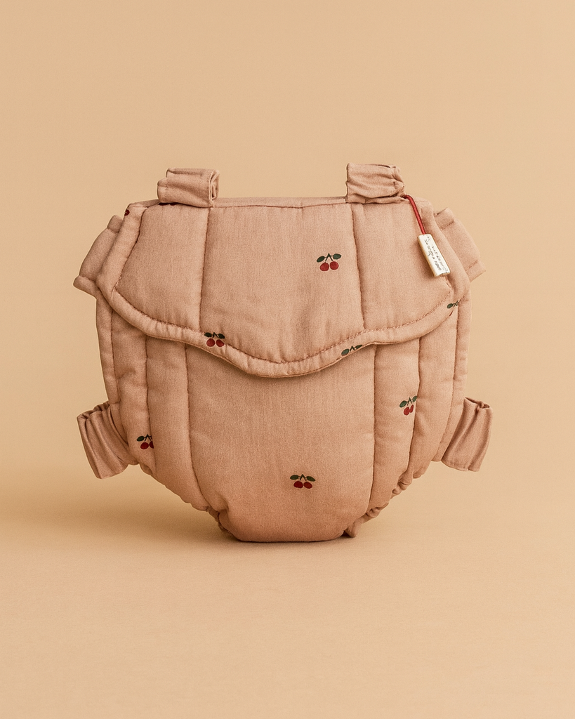 The Konges Sloejd Doll Carrier - Cherry Blush is a soft, padded cotton carrier in light brown with embroidered red cherries, shown upright against a matching beige background.