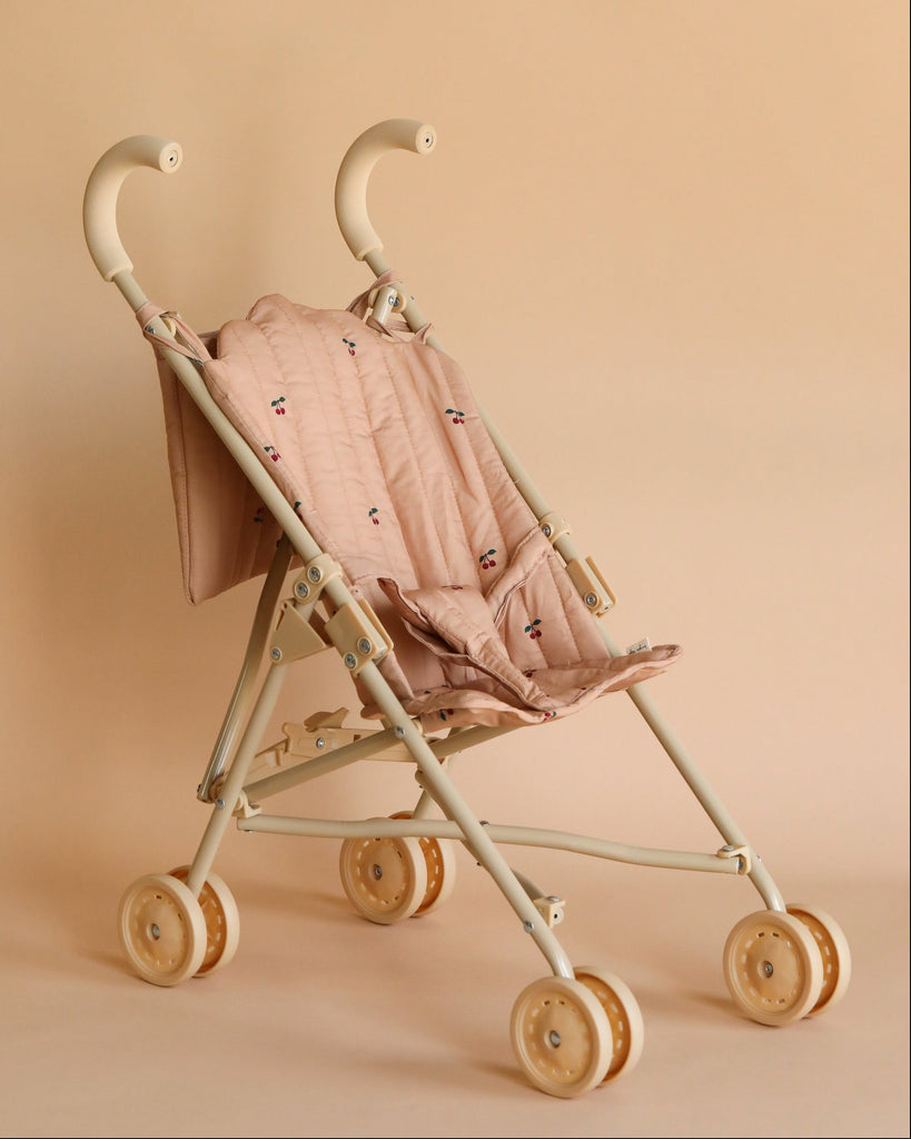 A Konges Sløjd doll stroller in cherry with a quilted fabric seat and beige double wheels, set against a soft beige background.