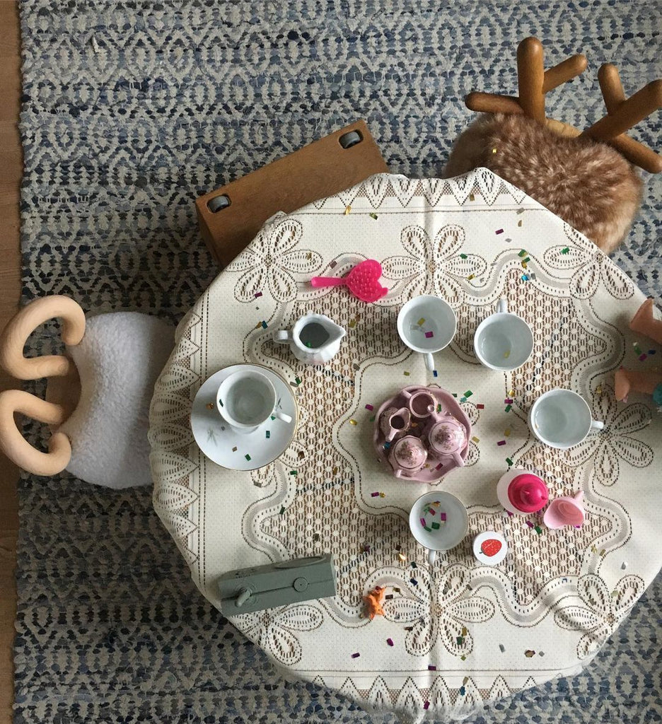 A child's tea party setup on a Faux Sheep Chair featuring a stuffed reindeer, miniature tea set with teacups, teapot, and plates, surrounded by scattered colorful beads and wooden toys