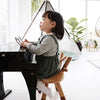 A young child sits on a Faux Bambi Chair made with fine materials, playing a small black piano in a bright, plant-filled room.