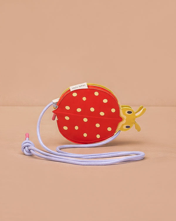 The Sticky Lemon Wallet Bag - Ladybug is a small red and yellow ladybug-shaped kids' PU leather bag with white polka dots and a lavender strap, shown on a plain beige background.
