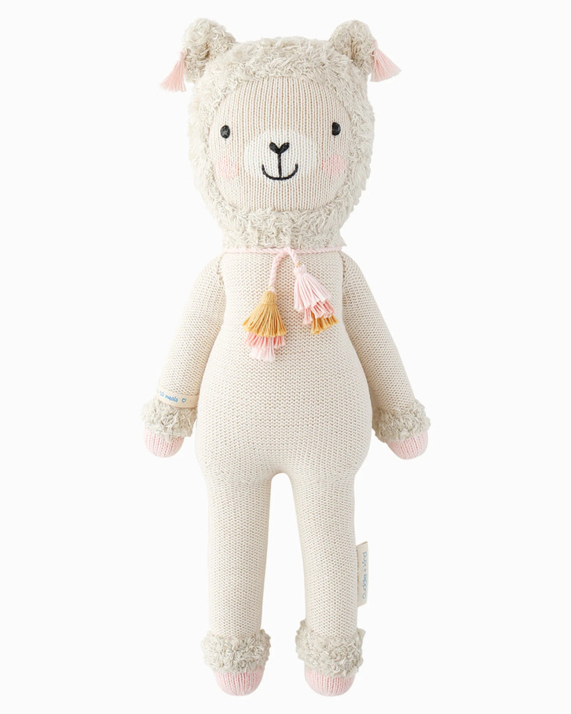 Cuddle + Kind Lola the Llama is a soft, hand-knit cream-colored doll featuring pink cheeks, tassels, and pink details on its ears, hands, and feet—a delightful fair trade toy for all ages.