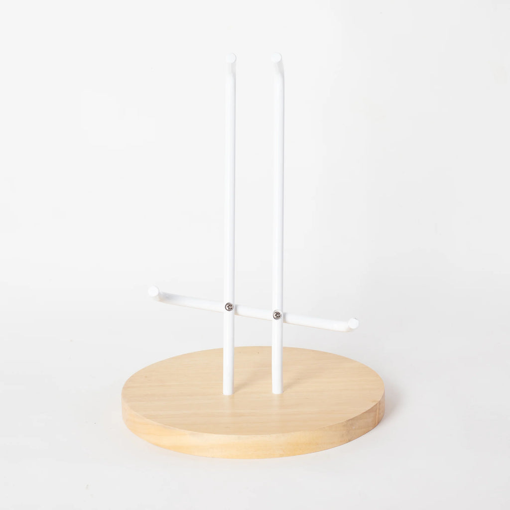 A minimalistic guitar stand with a circular wooden base and three vertical white rods, designed to hold items like necklaces and bracelets, isolated against a plain white background, similar in design to the Loog.