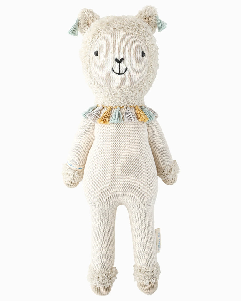 Cuddle + Kind Lucas the Llama is a hand-knit, fair trade doll with cream-colored fur, a smiling face, and a colorful tassel collar—an adorable handmade toy perfect for any child.