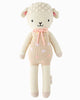 Cuddle + Kind Lucy the Lamb is a hand-knit, hypoallergenic doll with a cream body, beige face, pink cheeks, a pink bow, embroidered details, and pink spots on its sweater.