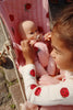 A child enjoys using the Konges Sloejd Doll Stroller - Ladybug, featuring ladybug designs and double wheels, to play with a baby doll. The stroller's removable fabric adds charm to their gentle outdoor play.