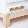 Close-up of the Milton & Goose Essential Play Kitchen, featuring white wood, light wood legs, and a branded wooden nameplate—handcrafted in the USA, perfect for imaginative play or as part of a wooden play kitchen collection.