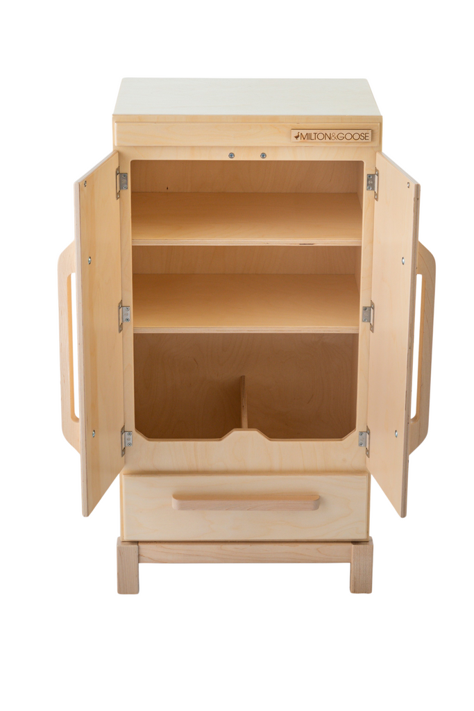 The Milton & Goose Essential Play Refrigerator, made in the USA, features a light wood finish, two open doors, bottom drawer, two interior shelves for play food, side handles, and a branded label on the top right corner—perfect for play kitchens.