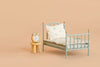 A small metal bed with pillows and a blanket sits next to the Maileg Stool Set, Mouse in Light Rose/Light Mint, which holds a silver alarm clock—all set against a beige background.
