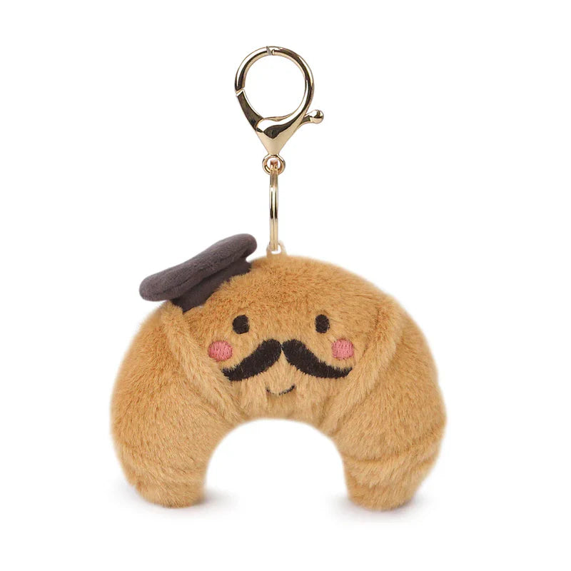 The Monsieur Croissant Keychain / Bag Charm features a plush croissant with a smiling face, pink cheeks, black mustache, and a tiny beret, attached to a gold clasp—ideal for cute keychain accessories or bag charms.