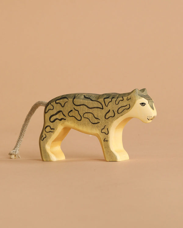 A Handmade Holzwald Snow Leopard with painted spots and a short yarn tail stands on a light brown surface against a matching background, showcasing the charm of sustainable toys.