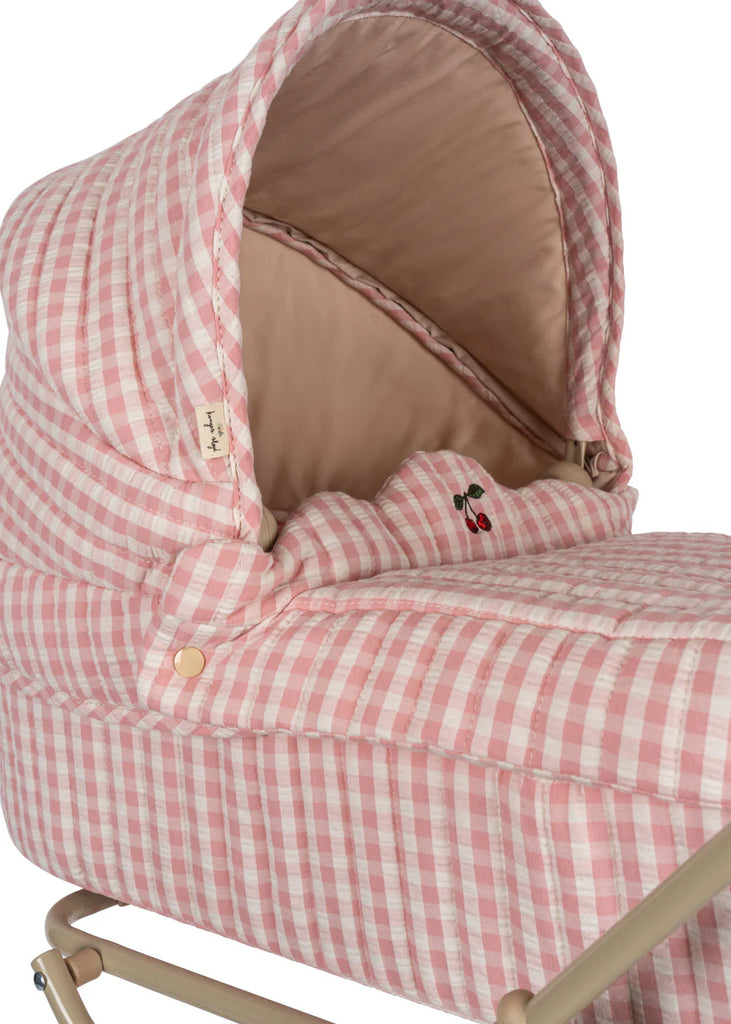 A close-up of the Konges Sloejd Doll Pram in Powder Pink Checkers, showcasing its pink and white checkered pattern with cherry embroidery details inside. The pram features quilted fabric, a padded mattress with a beige interior, and is mounted on a metal stand.