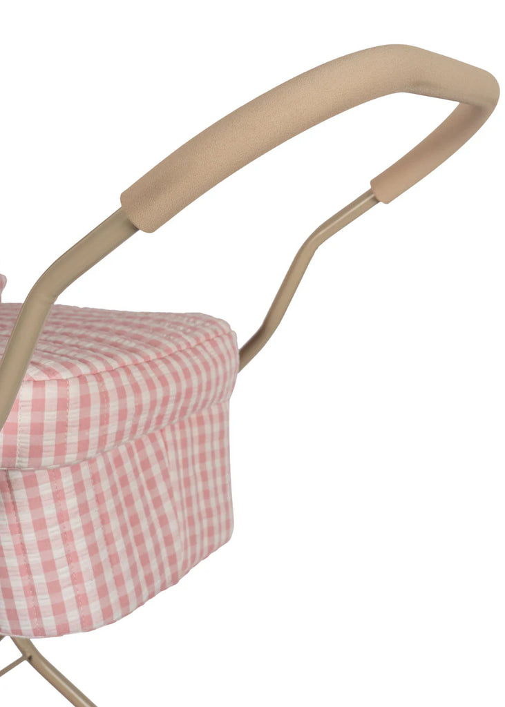 A close-up of the Konges Sloejd Doll Pram's handle reveals a beige foam grip, capturing the enchanting essence of a vintage-style stroller. The pink and white checkered fabric adds a quilted appearance, contributing to its soft and stylish aesthetic. The image emphasizes the handle's intricate craftsmanship.