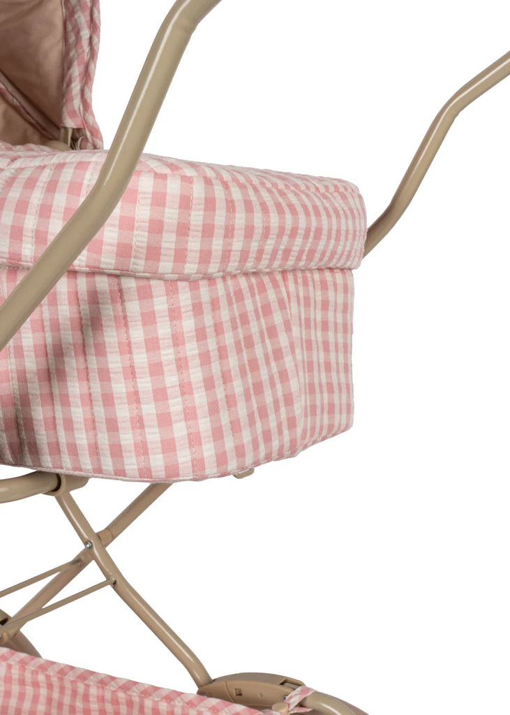 Close-up of the Konges Sloejd Doll Pram in Powder Pink Checkers, featuring its pink and white checkered quilted fabric. The light beige metal frame highlights the intricate fabric details on the side, complemented by a padded mattress.