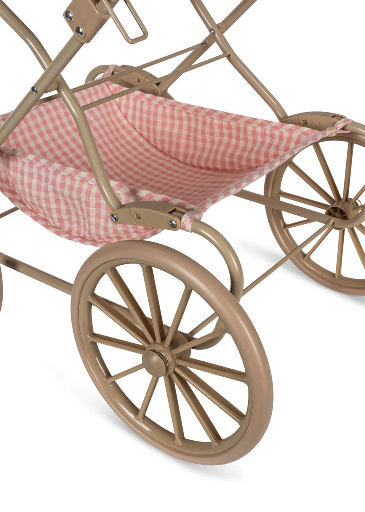 Close-up of the Konges Sloejd Doll Pram in Powder Pink Checkers, showcasing its vintage-style design with a beige metal frame and large wheels. The pram boasts a charming pink and white checkered quilted fabric seat that enhances its nostalgic appeal.