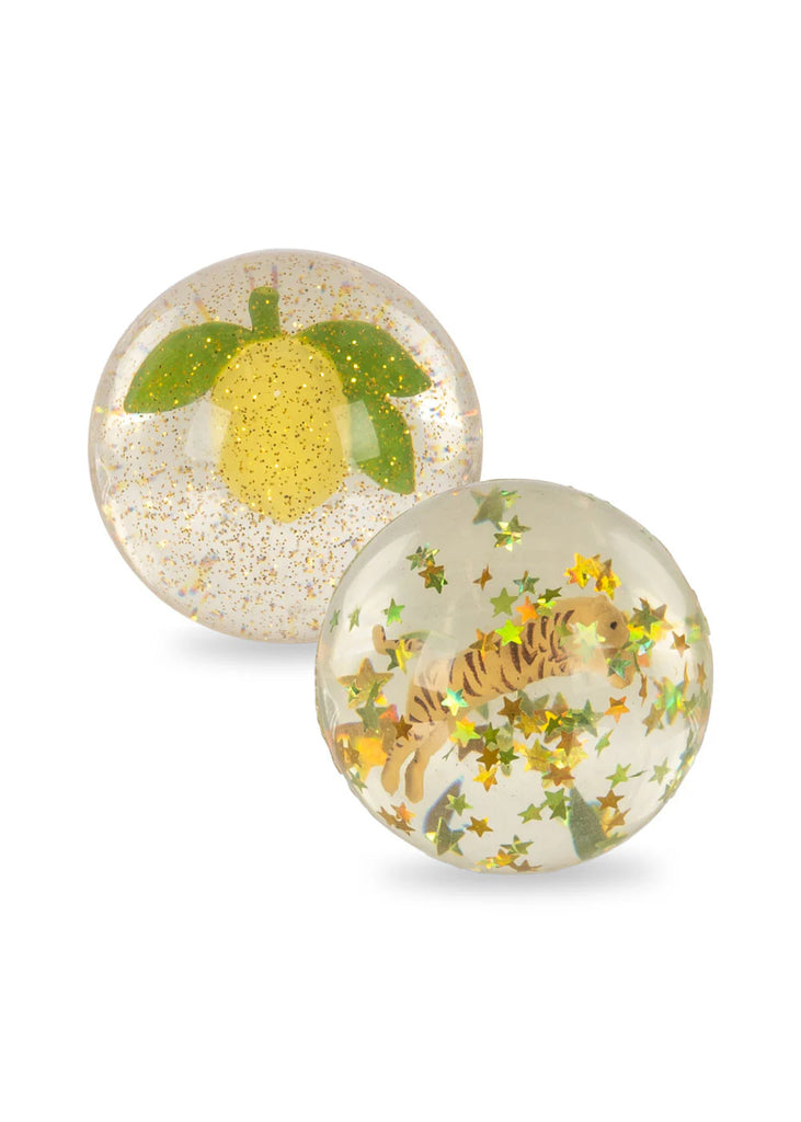 The Konges Sloejd - Bouncing Ball Set includes two round transparent balls; one showcases a yellow lemon with green leaves and gold glitter, while the other displays a tiger surrounded by green and gold star-shaped confetti. These captivating 3D designs reflect the playful elegance that defines Konges Sløjd.