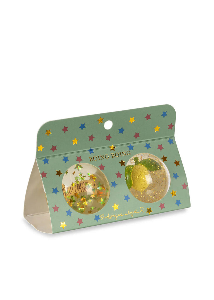 A green star-patterned package labeled "Konges Sloejd Glitter Bouncing Ball Set - Lemon & Tiger" displays two transparent bouncing balls with glitter and small decorations, visible through round windows on the front.