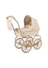 The Konges Sloejd Mini Doll Pram - Lemon has a vintage style with a cream-colored, quilted cover decorated with small bee patterns. It includes large spoked wheels and a matching handlebar bag, accompanied by a cushioned storage basket, offering an elegant and classic look. Delivery is expected in approximately one week.