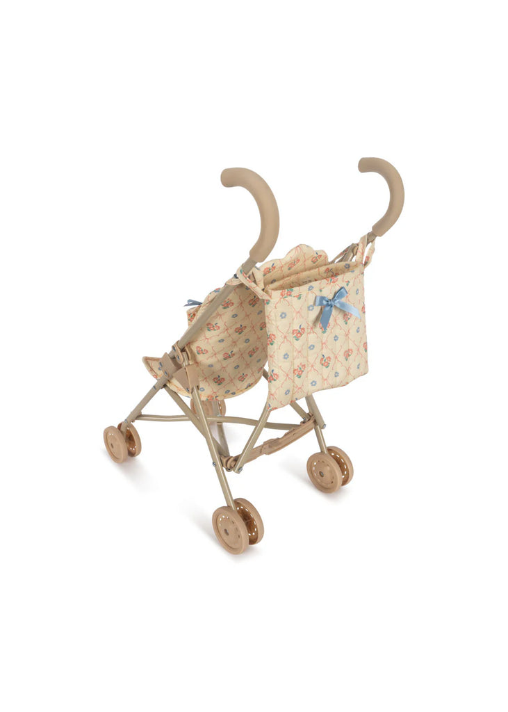 A compact and charming Konges Sloejd Doll Stroller - Fleur Decor, adorned with whimsical beige fabric patterns and a blue bow, featuring a robust beige frame with tan double wheels, all beautifully contrasted against a pure white background.