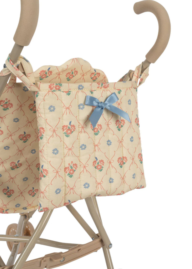 The Konges Sloejd Doll Stroller - Fleur Decor comes with a beige frame adorned with a floral-patterned fabric bag and a blue bow, featuring curved handles and double wheels for enhanced stability.