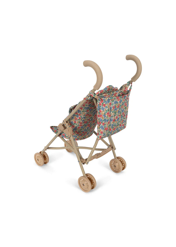 The Konges Sloejd Doll Stroller - Fiola features a beige frame with curved handles, four sets of double wheels, and a colorful floral Fiola print fabric seat and backrest, displayed on a white background.