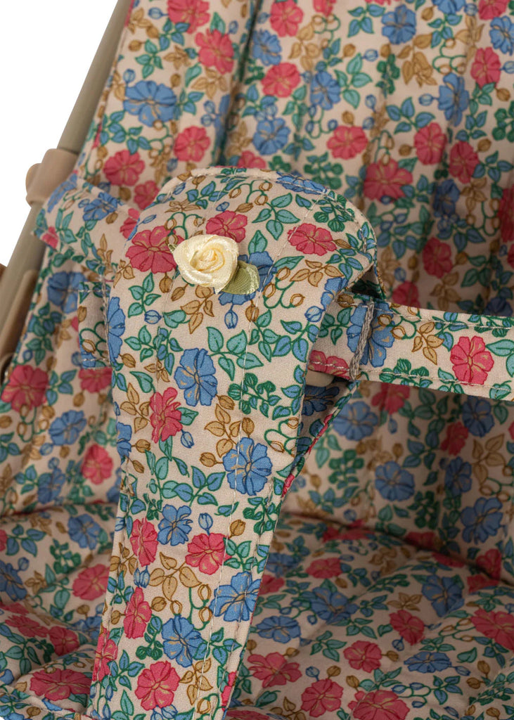 Close-up of the Konges Sloejd Doll Stroller - Fiola seat featuring a red, blue, and yellow Fiola print, with a small yellow fabric rose attached to the seat strap.