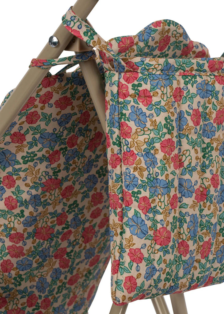 Close-up of the Konges Sloejd Doll Stroller - Fiola, showing its colorful quilted floral fabric in red, blue, yellow, and green with a ruffled top, draped over a beige metal frame.