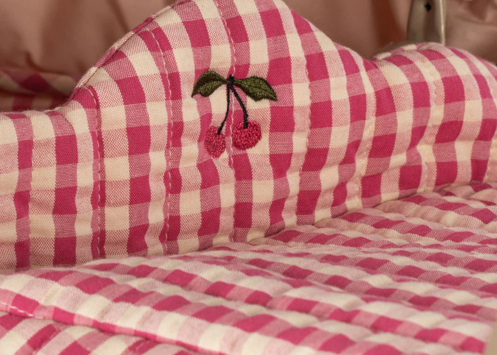 A close-up of the Konges Sloejd Doll Pram - Bubblegum Check shows pink and white checkered quilted fabric with an embroidered cherry motif of two red cherries and green leaves, evoking vintage charm.