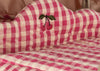 A close-up of the Konges Sloejd Doll Pram - Bubblegum Check shows pink and white checkered quilted fabric with an embroidered cherry motif of two red cherries and green leaves, evoking vintage charm.