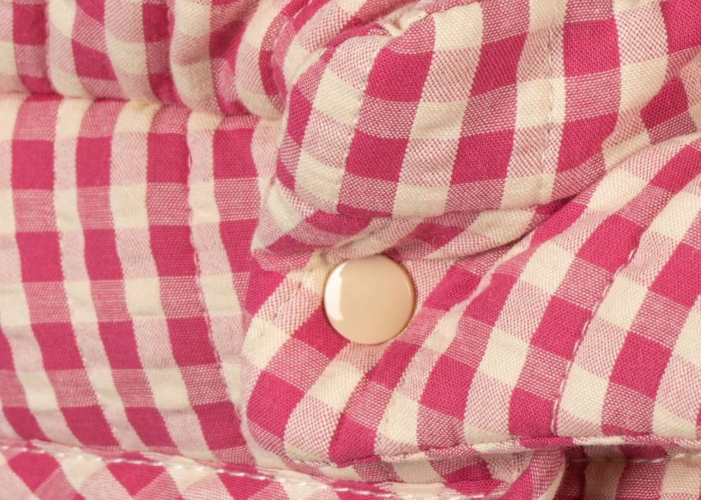 Close-up of the Konges Sloejd Doll Pram - Bubblegum Check shows quilted, pink and white checkered fabric with a cream snap button, featuring padded texture with visible folds and stitched seams.