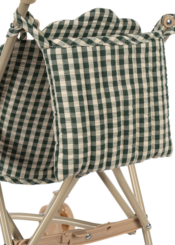A close-up of the green and white checkered storage pouch on the Konges Sloejd Doll Stroller - Smoke Pine Checker, attached to its beige metal frame.