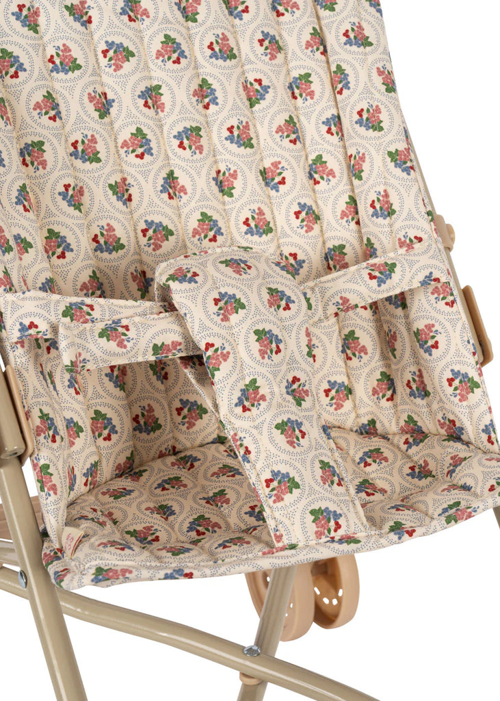 Close-up of the Konges Sloejd Doll Stroller - Verona Blues, showing beige floral and dot fabric in red, green, and blue, safety straps, double wheels, and a light tan metal frame.