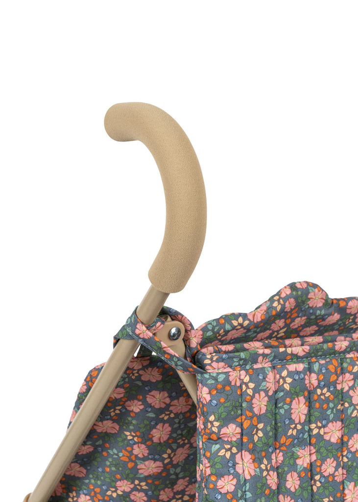 Close-up of the Konges Sloejd Doll Stroller - Kyoto handle with a beige foam grip. The stroller fabric has a vibrant floral pattern in pink, orange, and white on a blue background. White backdrop.