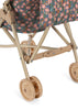 Close-up of the lower part of the Konges Sloejd Doll Stroller - Kyoto in beige, featuring double wheels and a floral fabric seat with pink and orange flowers on a dark background.