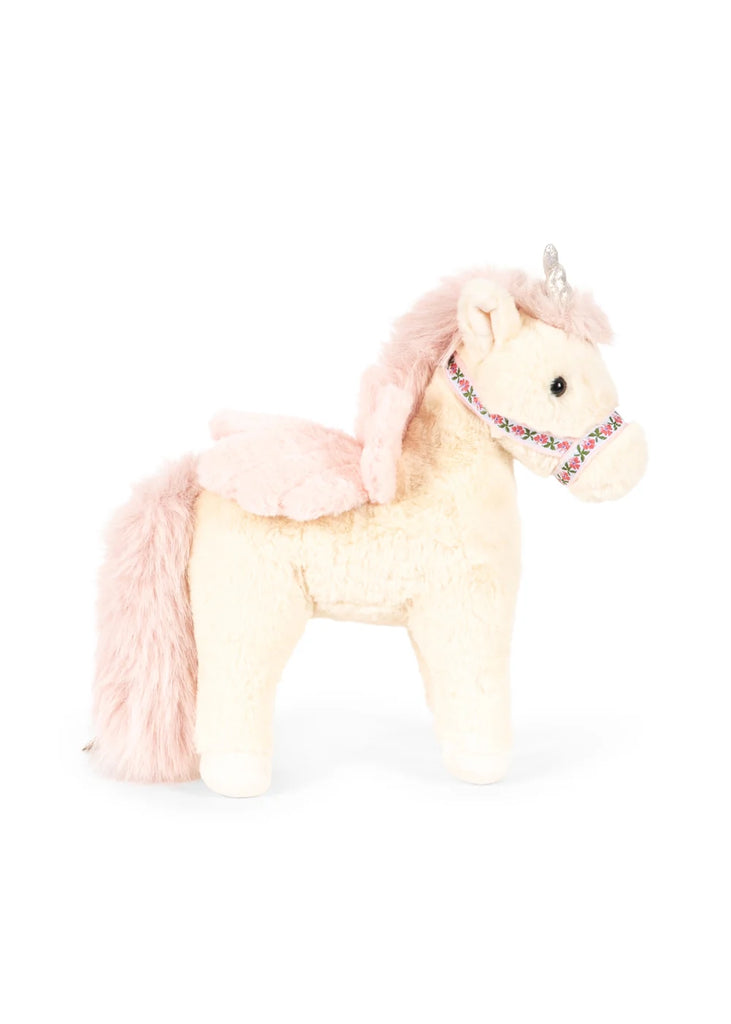 The Konges Sloejd Starlight Unicorn Stuffed Animal features cream-colored fur, a pink mane and tail, pink wings, a silver horn, and a floral-patterned harness, and is shown standing upright on all four legs.