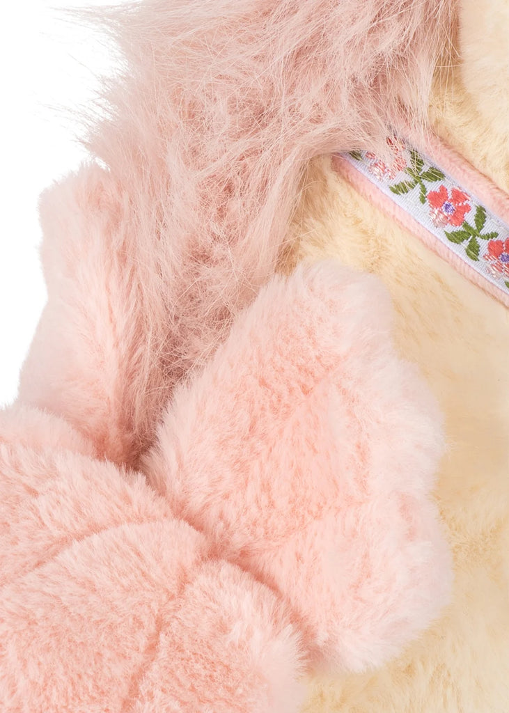 Close-up of the Konges Sloejd Starlight Unicorn Stuffed Animal, featuring soft, light pink fur, delicate pink wings, a large bow, and a floral-patterned ribbon around its neck. The blurred background accentuates the plush fabric’s gentle textures.