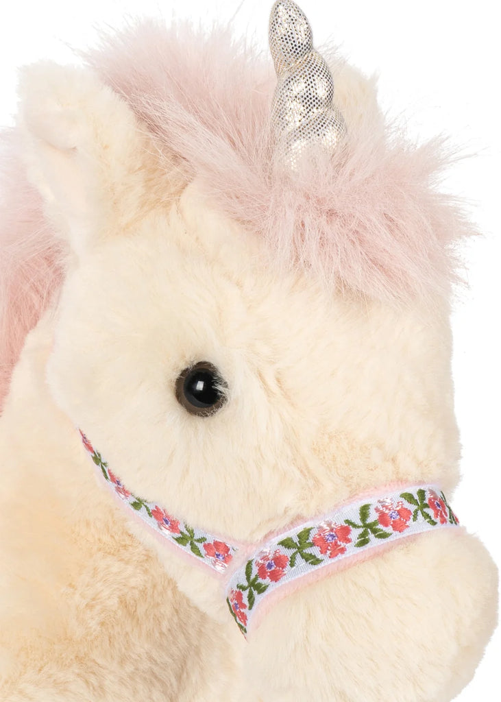 The Konges Sloejd Starlight Unicorn Stuffed Animal features cream fur, a pink mane, and a shiny silver horn. This adorable plush toy is adorned with delicate pink wings and wears a ribbon decorated with pink flowers and green leaves around its snout.