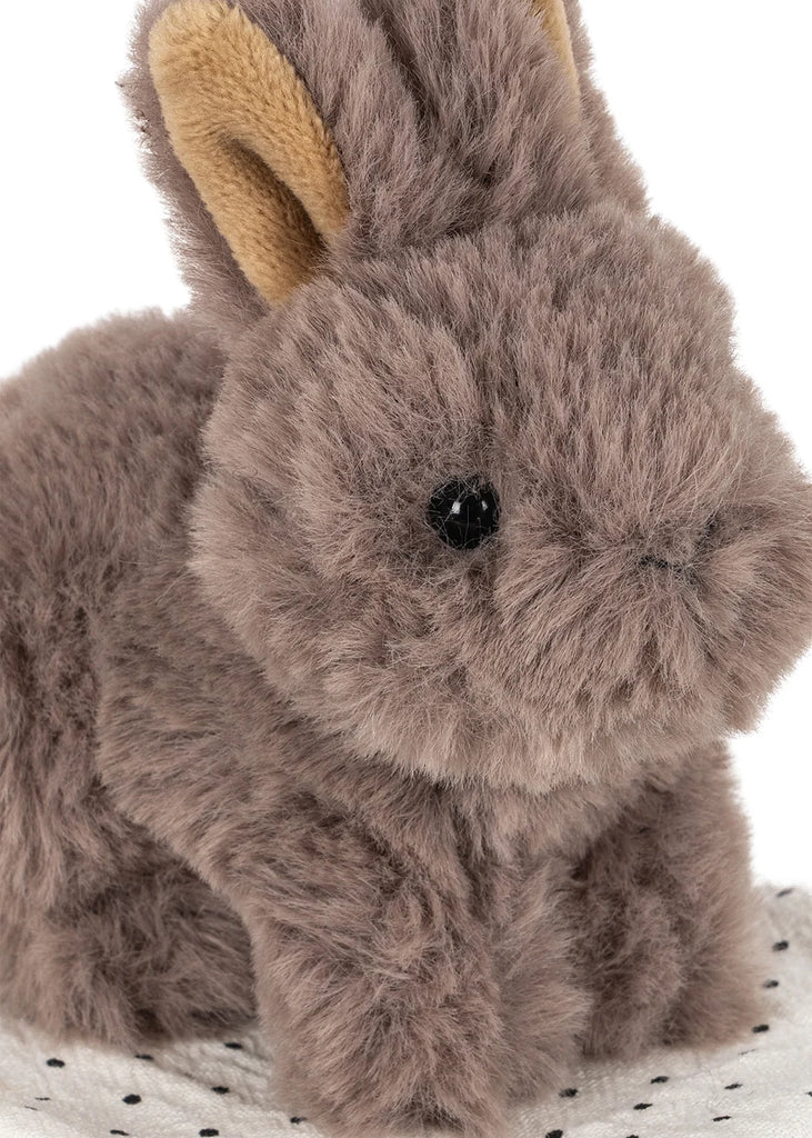 A close-up of the Konges Sloejd Take Care of Me Animals - Bunny shows its fluffy brown fur, black eyes, and tan inner ears as it sits on a white textured surface. This adorable plush bunny seems to say, “take care of me,” inviting everyone to cuddle and cherish this charming mini toy animal.