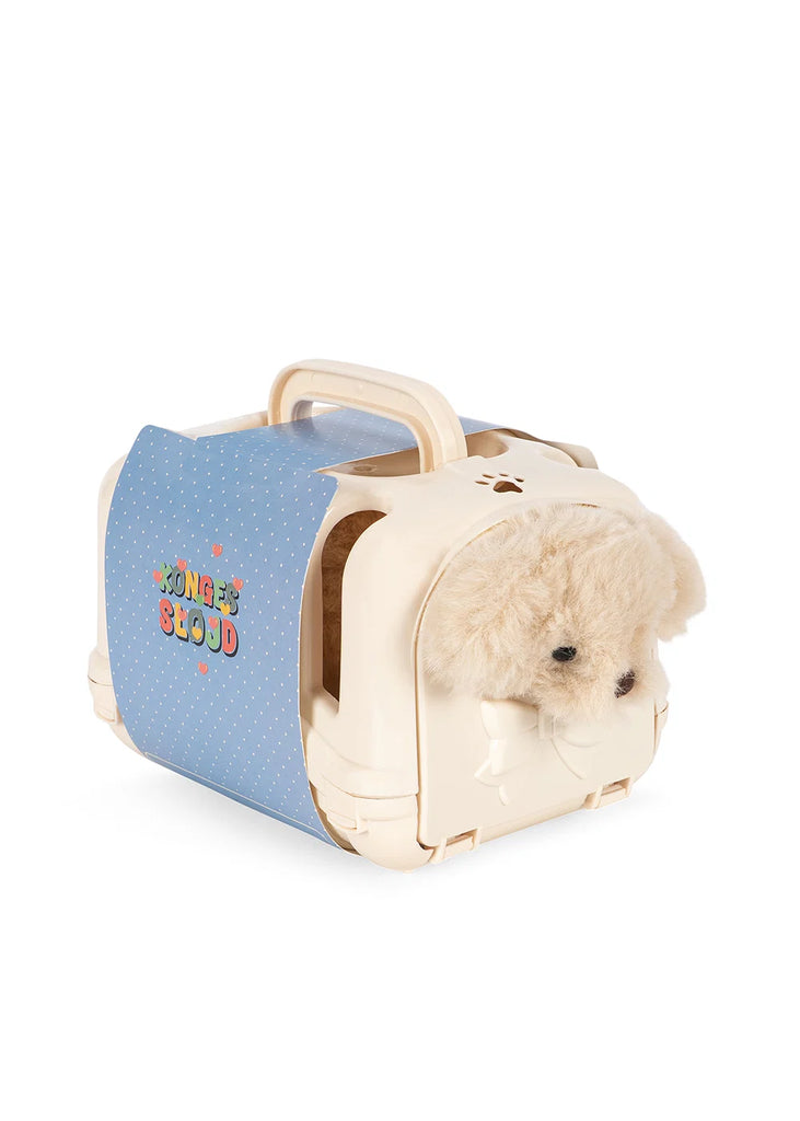A mini Konges Sloejd Take Care of Me Animals Dog plush peeks out from a small cream-colored plastic pet carrier with a blue polka dot cover and handle, ready for you to care for it.
