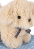 A Konges Sloejd Take Care of Me Animals - Dog plush, featuring soft beige fur, black eyes, a brown nose, and a gray bow around its neck, sits on light blue fabric with white polka dots, gazing upward in an endearing pose.